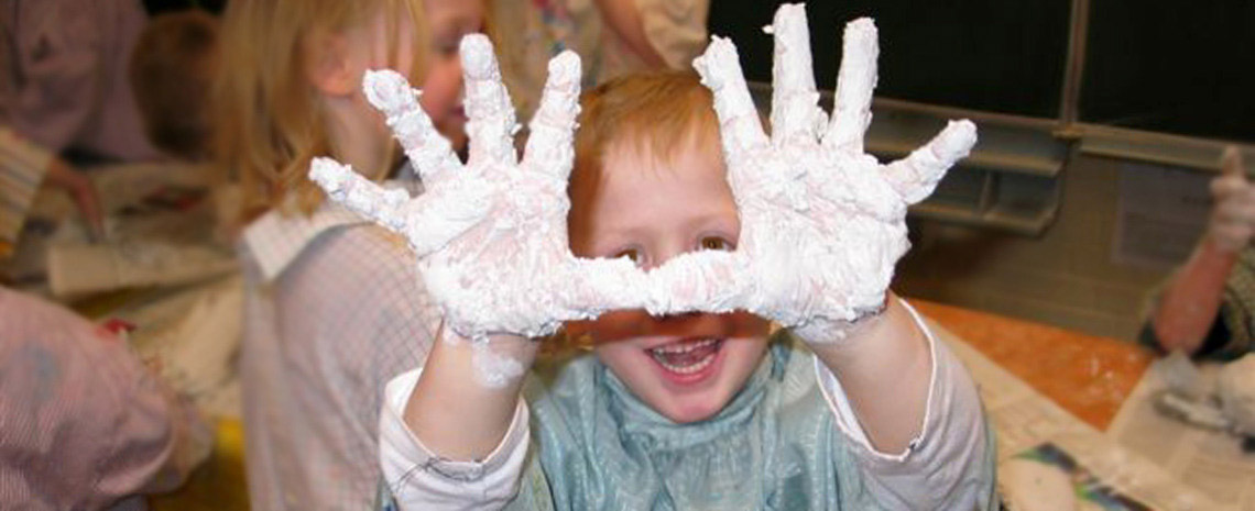 lachende Kind streckt seine Hände in die Kamera. Es wird gebacken und die Hände sind voller Teig