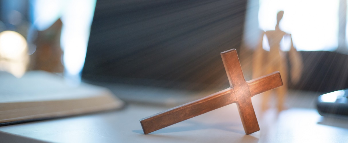 Foto im Büro, Schreibtisch mit Kreuz, welches von der Sonne beleuchtet wird